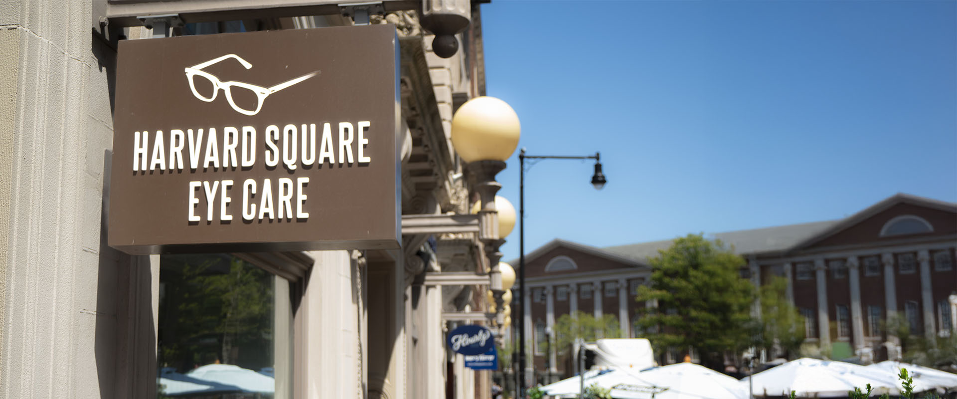 The image shows a storefront with a sign that reads  Harvard Eye Care  on a building with architectural details, situated in an urban environment with clear skies and sunlight.