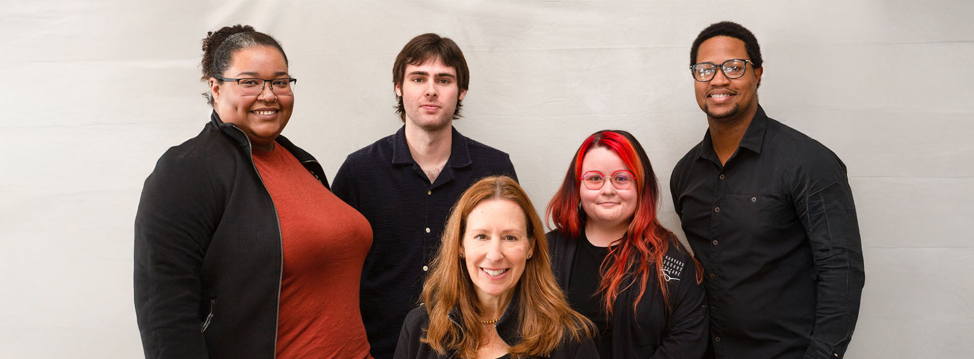 The image shows a group of five individuals posing together for a photograph they appear to be a diverse team, possibly colleagues or friends, with one individual standing prominently in front of the others.