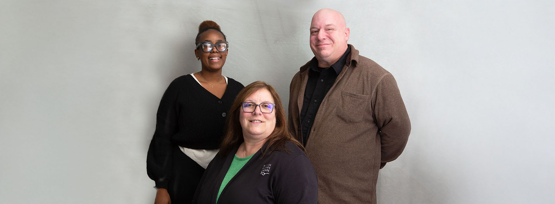 The image features three individuals standing side by side against a plain background.