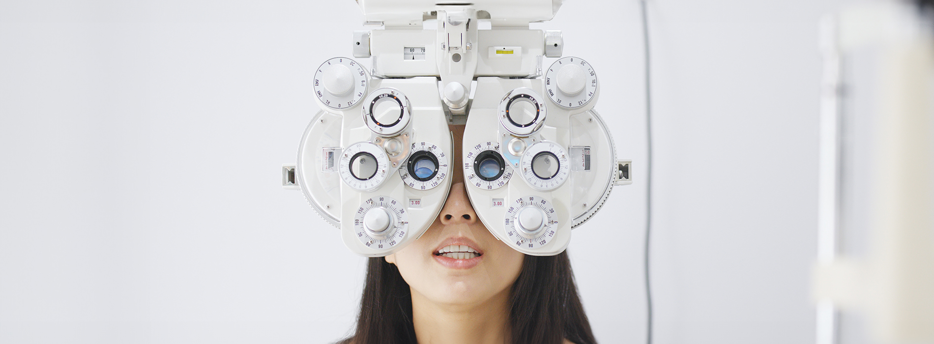 A woman wearing glasses is looking through an optical device, likely a microscope or telescope, with a focus on her eyes, set against a white background.