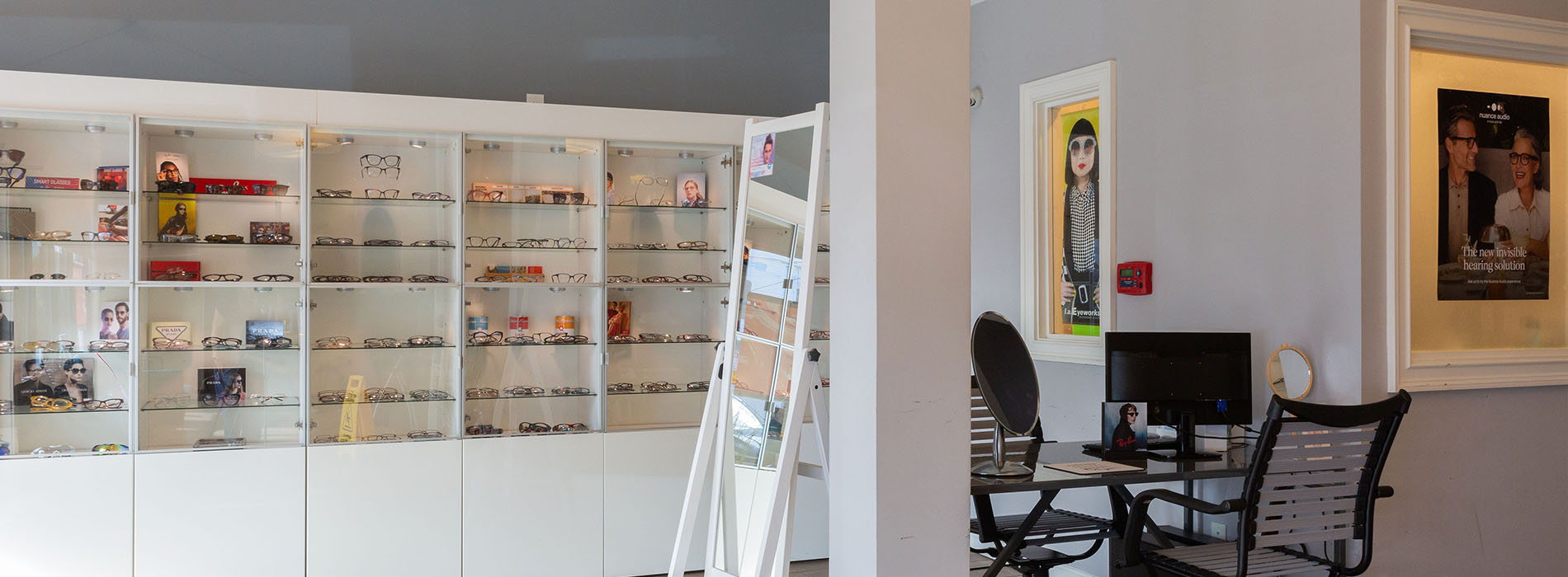The image shows a room with a large display case containing various items, including eyeglasses and books, and a collage of smaller images on the wall above the display case.