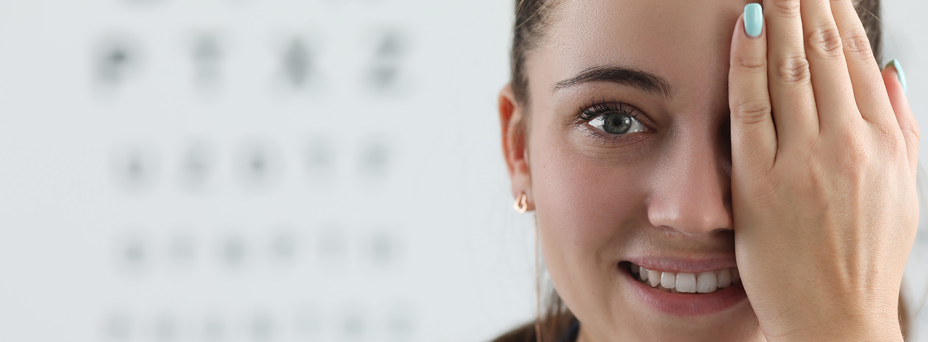 A young woman with her hand on her face, possibly in surprise or concern, against a blurred background that appears to be an eye chart.