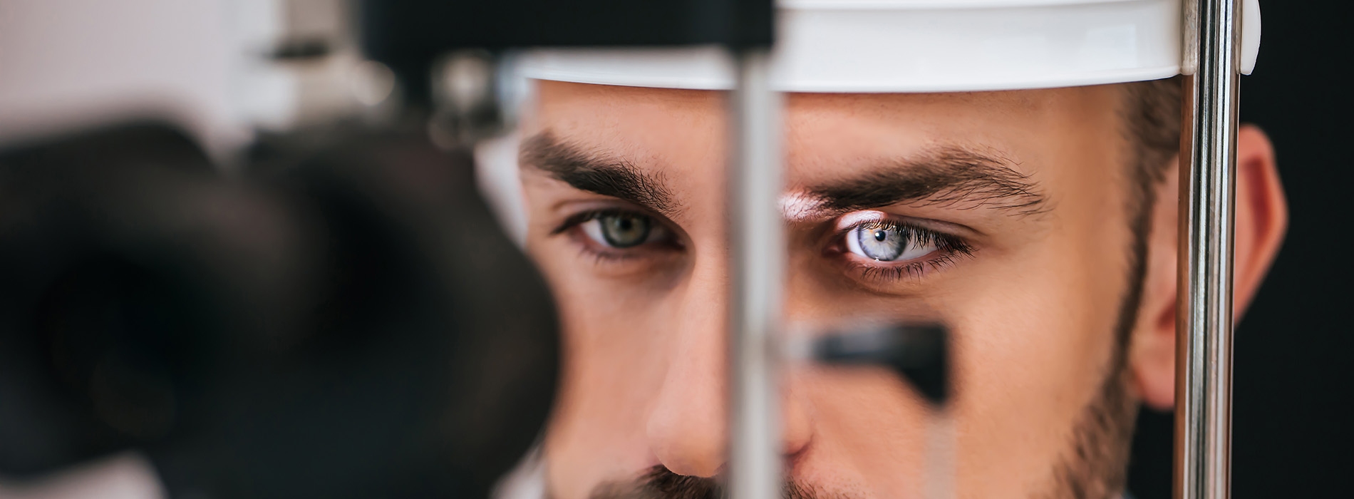 The image shows a man with a beard looking into a camera lens, possibly from a security or surveillance context, given the presence of a metal detector and the focus on his face.