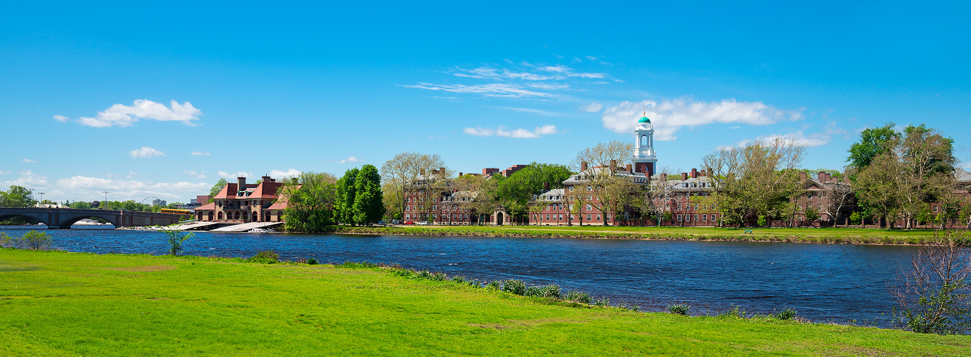 The image depicts a serene landscape featuring a river with a bridge, a town on the far side, and a clear blue sky above.
