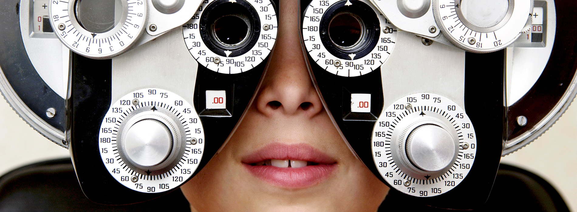 The image shows a person wearing an eye exam machine, with their eyes obscured by the device, creating a surreal effect where only the eyes are visible from behind while the rest of the face and body are hidden.
