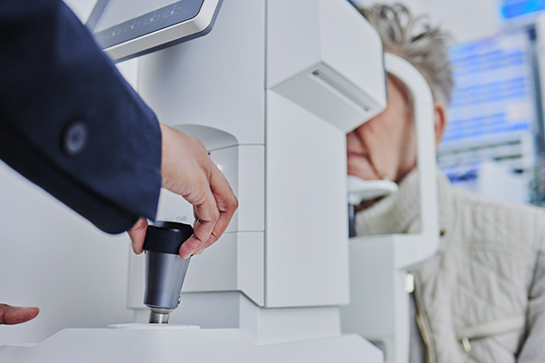 The image shows a person interacting with a piece of medical equipment, possibly an ophthalmologist using a device to measure eyesight or perform an eye examination.