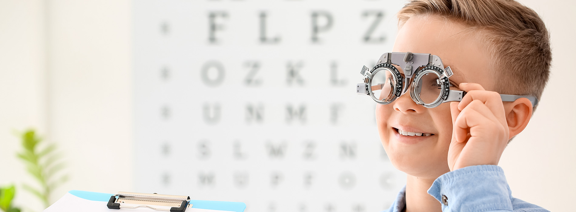 A young boy wearing glasses with a magnified view of an eye chart behind him.