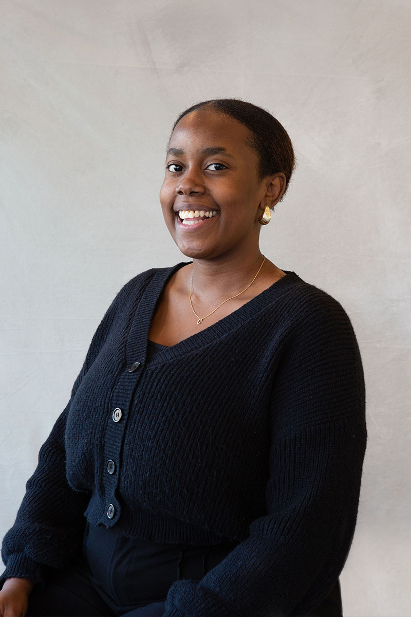 The image shows a person sitting and smiling at the camera, with a neutral background.