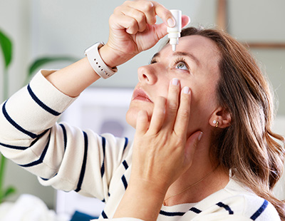 A woman applying eye drops with an eyedropper.
