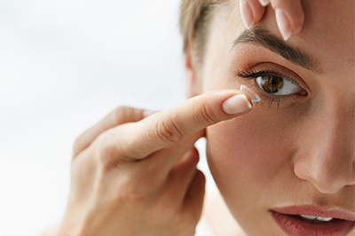A woman applying makeup with her eyes closed, focusing intently on the task at hand.